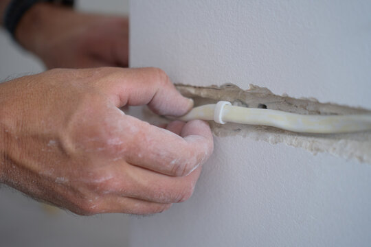 Hand placing cable conduit into channel cut in wall. Concept of home renovation