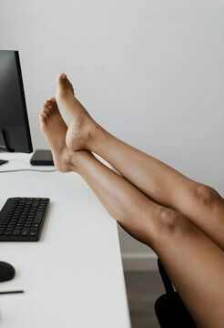 Bare feet and legs resting on a white office desk with a keyboard and monitor relaxation and comfort at work, the scene a sense of personal well being and stress relief in a modern minimalist