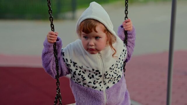 Child enjoying a swing at an outdoor playground, gripping the chains and moving through a playful moment of childhood recreation