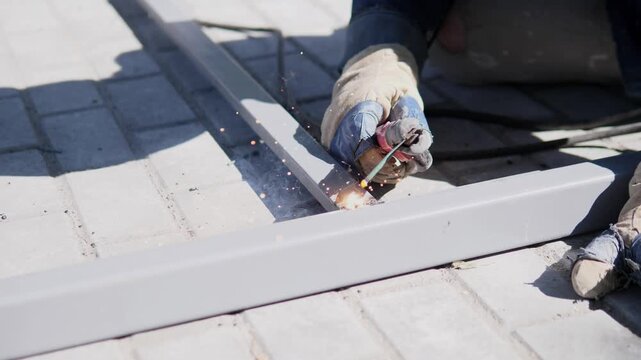 Gloved roofer works along white metal trim over corrugated roof panels, grinding at contact point with bright sparks, careful exterior repair under strong sunlight, with roofing, repair, maintenance