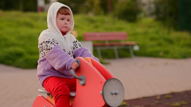 Child playing on a spring rocker in a park, moving from seated riding to standing while enjoying outdoor playground activity