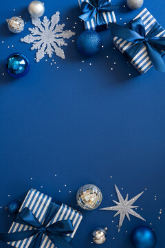 Merry Christmas and Happy New Year blue holiday flat lay with wrapped gift, ornament, snowflake and bow on vertical blue wallpaper