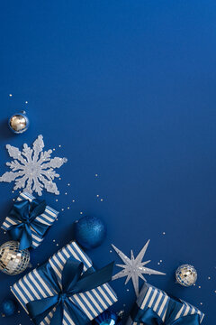 Blue holiday gift scene with striped presents, ornaments, snowflake and festive New Year decorations on vertical dark blue empty space