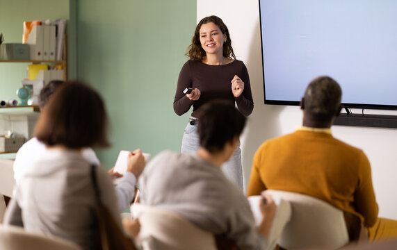 Young woman lecturer speaks to audience of listeners, shares knowledge, communicates with listeners. Language courses, education and exam preparation, lectures and practical classes at school..