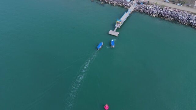 Aerial drone view of boats navigating to and from the Isla de la Piedra pier in Mazatl&aacute;n, Sinaloa, Mexico. One boat approaches the pier while another moves away across the calm waters