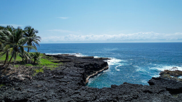 Rocky coastline at Ilh&eacute;u das Rolas, S&atilde;o Tom&eacute; and Pr&iacute;ncipe, featuring volcanic lava formations, Atlantic waves and coconut palms overlooking the ocean.
