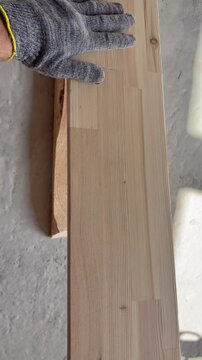 a worker's gloved hand checking the smoothness of a sanded wooden board. Carpentry, woodworking, or home renovation