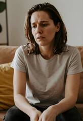 Fototapeta premium Distressed young woman with a worried expression sitting on a couch, mental health and emotional struggle