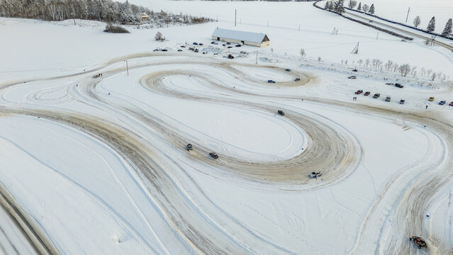 Aerial view of cars driving on a snow-covered ice track with tire tracks and a nearby building in Rakvere, Laane-Viru County, Estonia.