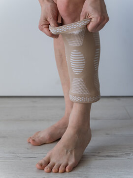 A Caucasian woman suffers from knee pain and wears a supportive elastic knee brace.