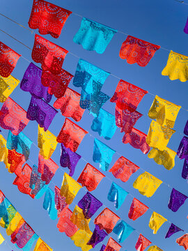 View of colorful Papel Picado banners hanging against a clear blue sky in Izamal, Yucatan, Mexico.