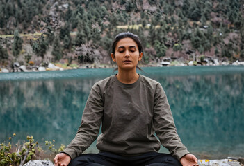 Fototapeta premium Young woman meditating outdoors by a serene lake with eyes closed, practicing mindfulness and mental well being in nature