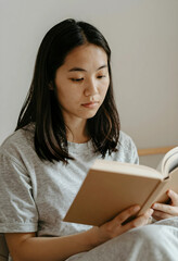 Naklejka premium Young asian woman reading a book at home, education and learning concept, leisure and relaxation activity