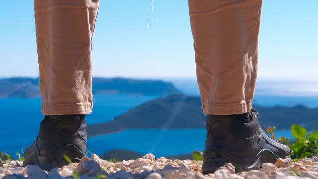 Person urinating on mountain top with sea. Close-up of a person's legs while urinating on rocky ground after a hike, with a sea and island landscape in the background, representing a moment of relief