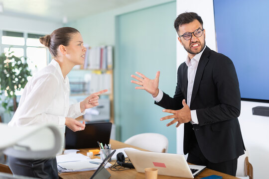 Office employees stand near table and actively argue with each other, they are angry at the inconsistent budget and the wrong project deadlines. Man and woman arguing in the middle of the office
