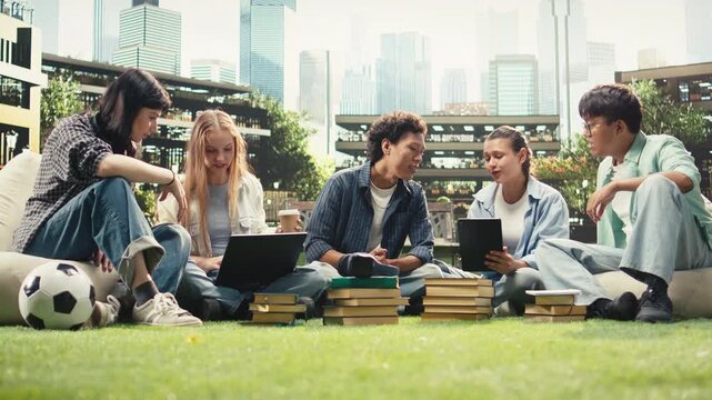 Portrait shows diverse students sitting on a university campus lawn for group study collaboration, reading notes from a laptop and books, with international peers in an academic environment.