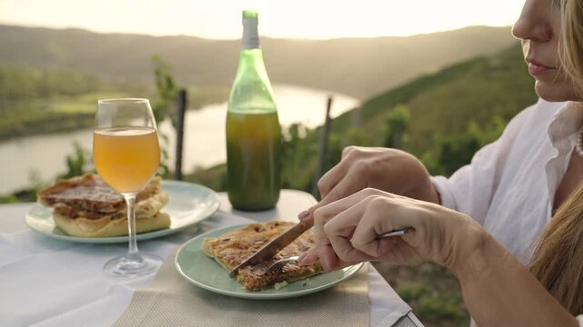 Young Woman Enjoys Federweisser young wine served with Onion tart Zwiebelkuchen. Rhine Valley terraced vineyards Germany