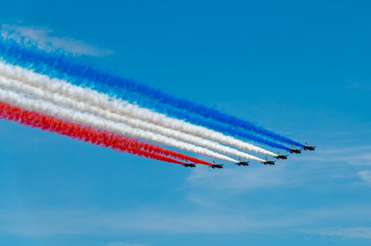 Jets fly formation leaves parallel tricolor smoke trails. Seven Alpha Jets fly diagonally through clear sky with red, white and blue plumes widening behind.