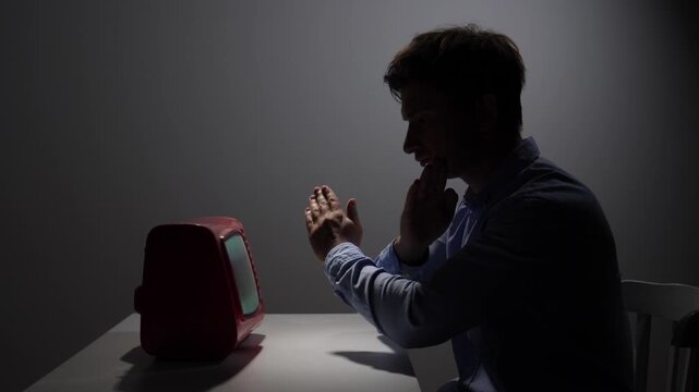 Man with clasped hands is worshipping a small, vintage red television set, symbolizing media obsession, misinformation, and the cult like influence of technology
