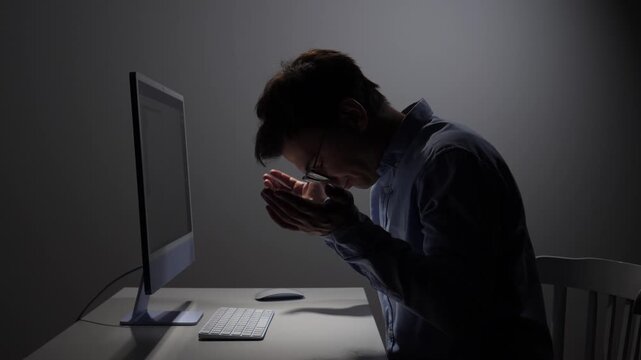 Young man working on computer at night showing frustration and stress, experiencing technology issues or a difficult task in a dimly lit office environment
