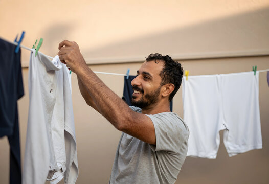 Smiling man hanging white laundry on a clothesline outdoors, domestic chores and household duties concept, the man is happy and content while performing this common household activity