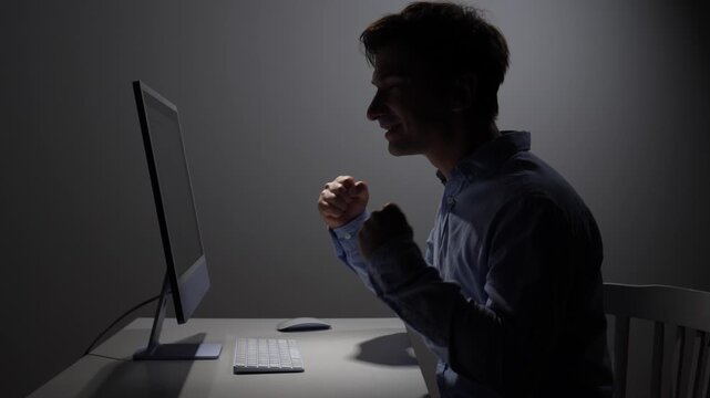 Man feeling excited and achieving success while working on a computer screen in a dark office, demonstrating dedication, victory, and late night productivity