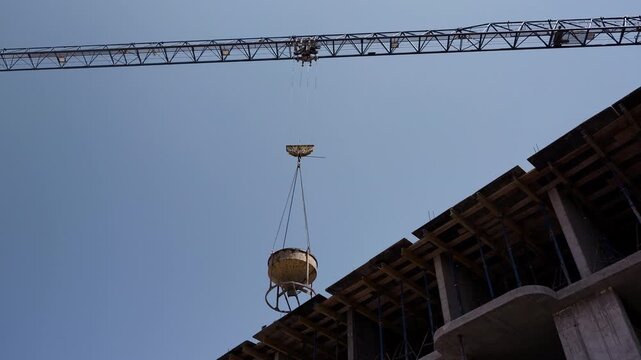 Tower crane lowering concrete bucket onto unfinished building wide shot
