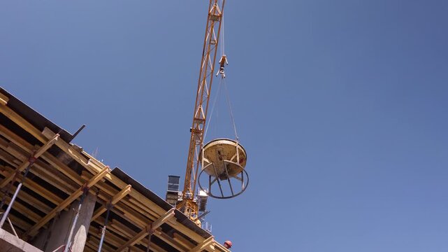 Tower crane lifting concrete bucket above building construction site low angle