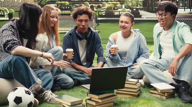 Diverse peers gather on the grass at a university campus for group study session, reviewing coursework notes and sharing ideas together.