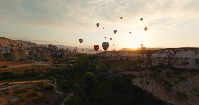 FPV aerial view of colorful hot air balloons floating over the unique fairy chimney rock formations of Cappadocia at sunrise in Turkiye.