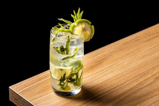 Bartender making a refreshing Mojito cocktail with fresh mint and lime on a wooden bar counter against a black background.