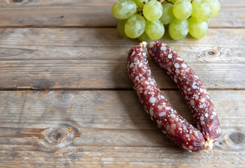 Obraz premium Two dry cured sausages and green grapes on a rustic wooden table, gourmet food and snack concept, this gourmet food combination suggests a delicious snack or appetizer