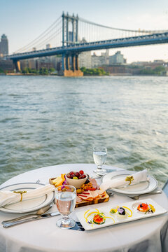 Dining with a view of the Manhattan Bridge on the East River in New York City. People enjoy a meal by the water with a view of the Manhattan Bridge in New York City.