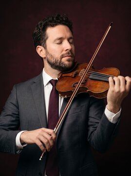 Professional violinist playing wooden violin. Elegant male musician in suit performing classical music. Orchestral artist with eyes closed.