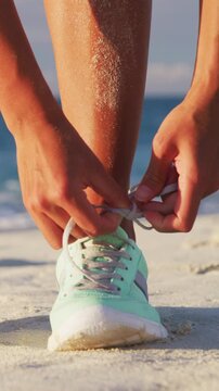 Runner woman tying laces of running shoes preparing for beach jogging. Closeup of hands lacing cross training sneakers trainers for cardio workout. Raw unedited vertical video of real woman model.