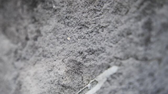 Slow horizontal camera pan from right to left showcasing the intricate details, roughness, and natural texture of a rugged stone surface.