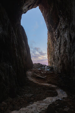 View of the natural tunnel through Torghatten mountain with a stone path leading to the opening, framed by dark rock walls in Bronnoy Municipality, Nordland, Norway.