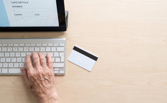 Elderly woman typing credit card details into computer to pay online shop purchase