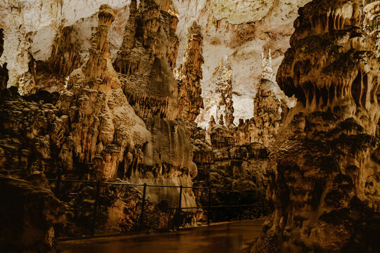 View of the impressive limestone formations and stalagmites inside Postojna Cave with a pedestrian walkway and metal railing in Postojna, Postojna, Slovenia.