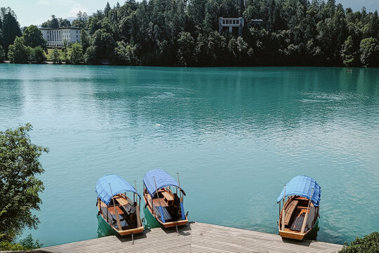 View of traditional wooden pletna boats with blue canopies docked at a wooden pier on the turquoise waters of Lake Bled, Bled, Radovljica, Slovenia.