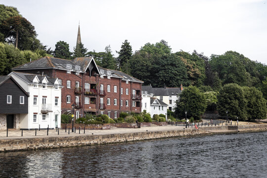 View of the historic riverside buildings with red brick facades and a white house along the Exe River promenade in Exeter, England, United Kingdom.