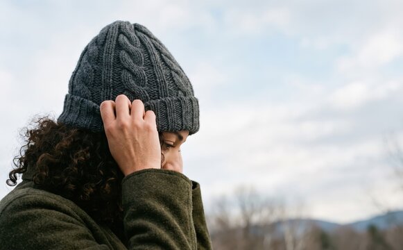 Young adult woman with curly hair wearing a gray knitted beanie outdoors in winter