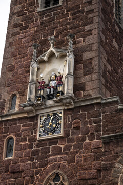 View of the historic St Petrock's Church clock tower featuring the ornate quarter jacks and clock face set into the red sandstone masonry in Exeter, England, United Kingdom.
