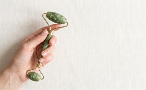 Woman holding a green jade facial roller for skin care and wellness massage