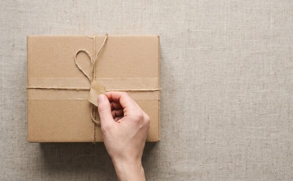 Unboxing a wrapped brown cardboard parcel gift box with string on linen background for delivery concept