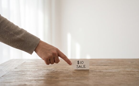 Woman pointing at a ten dollars sale tag on a wooden table representing a discount and retail offer