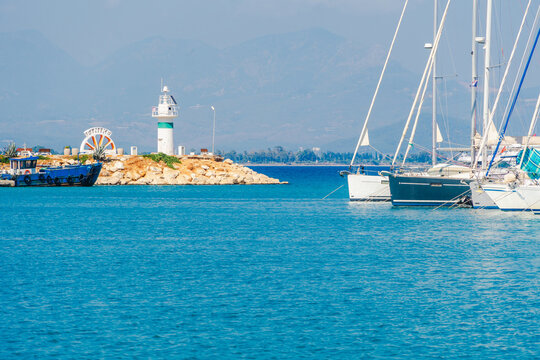 White lighthouse on a harbor islet with yachts anchored on brigh