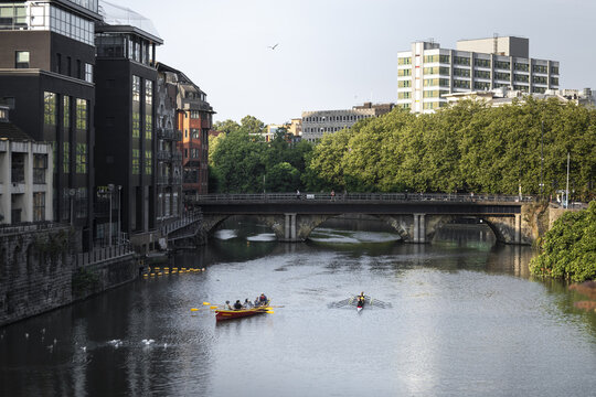 View of rowers in small boats on the River Avon passing under a stone bridge in the city center of Bristol, England, United Kingdom.