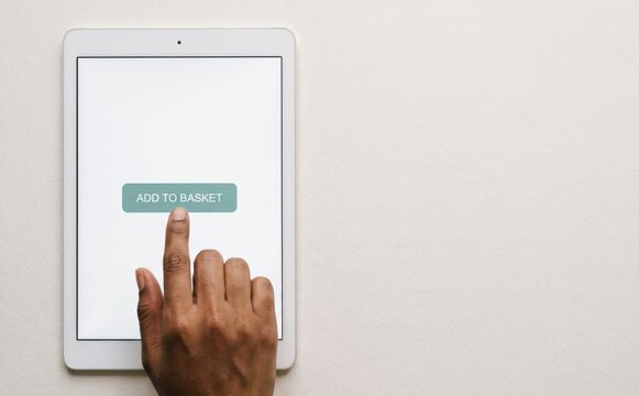A hand tapping an add to basket button on a tablet screen, symbolizing online shopping, e-commerce, and digital retail technology.