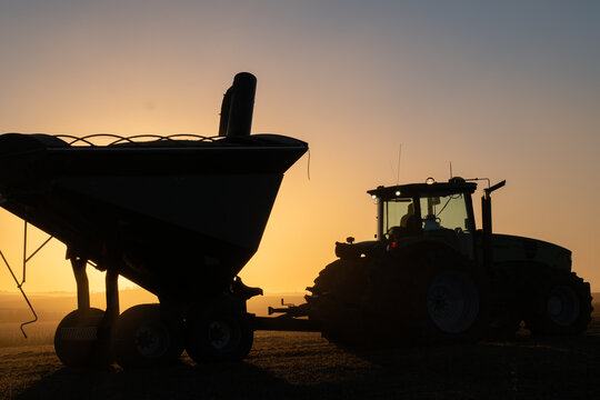 Agricultural tractor pulling grain cart during soybean harvest at sunset